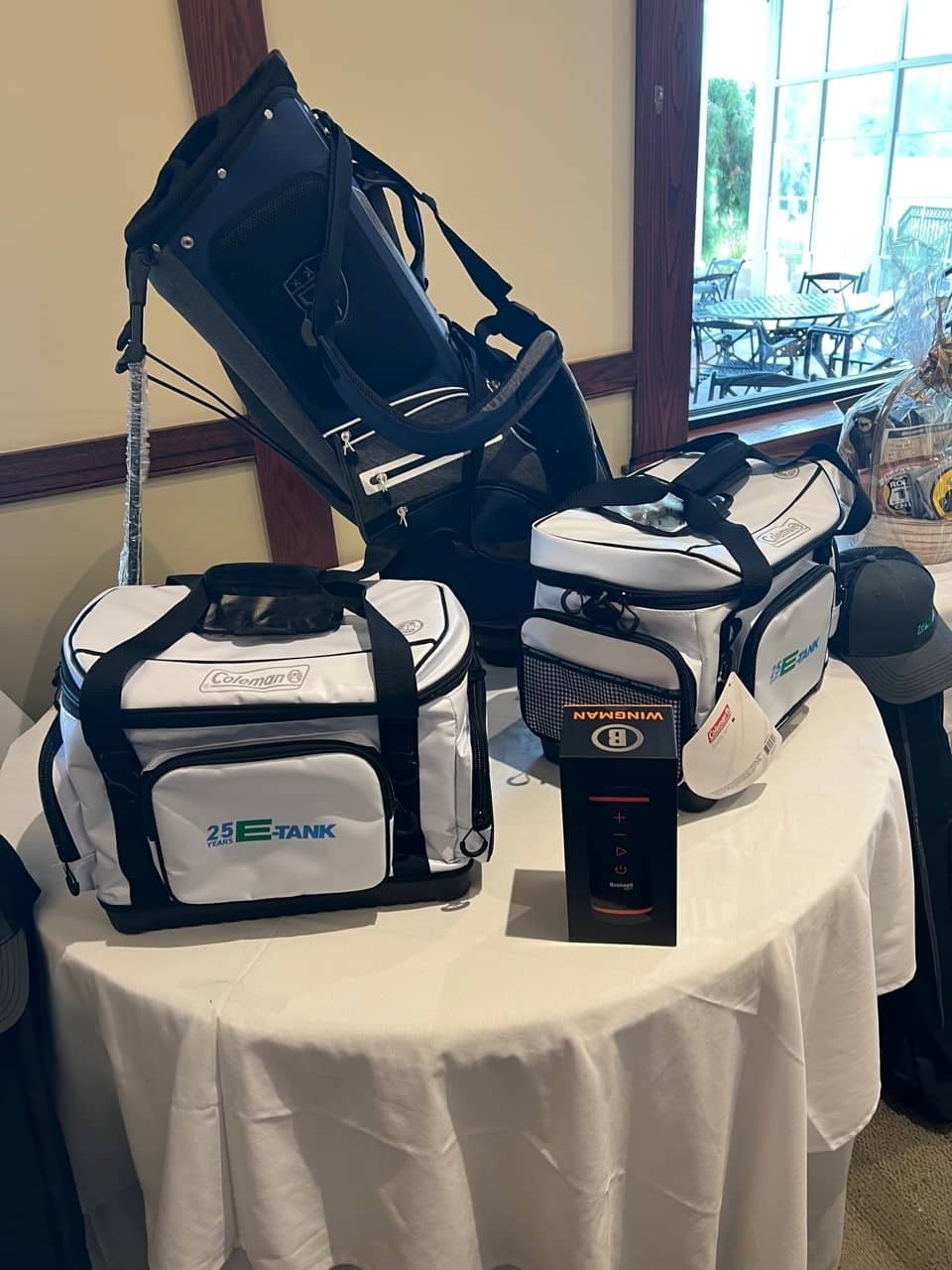 Golf bags and E-Tank branded Coleman coolers arranged as raffle prizes for the E-Tank Classic charity golf event, celebrating E-Tank’s 25th anniversary.