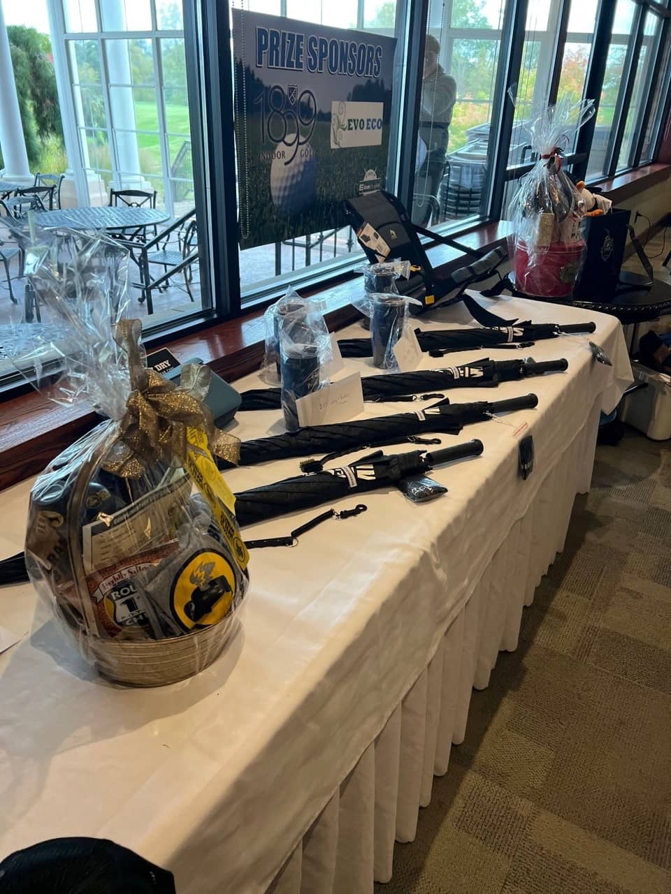 Raffle table with golf umbrellas, tumblers, and prize baskets at the E-Tank Classic charity golf event, showcasing sponsor support and prize donations.