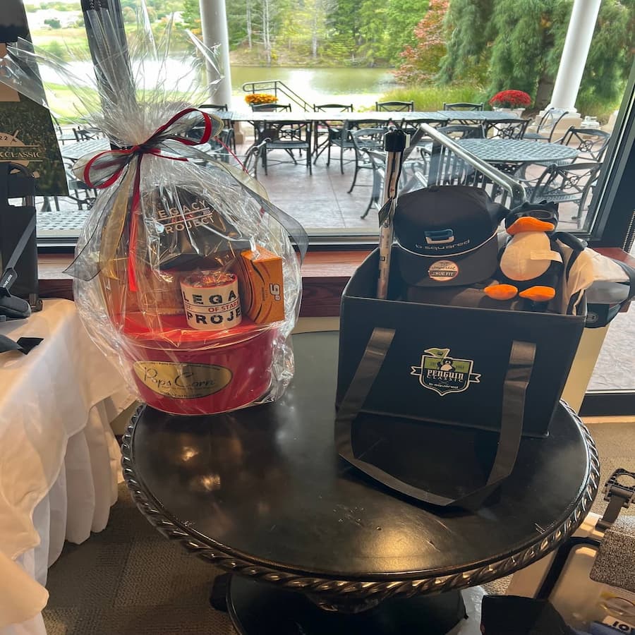Raffle prizes displayed at the E-Tank Classic golf outing, including a Legacy Project gift basket and a Penguin Classic golf prize pack, supporting local community initiatives.
