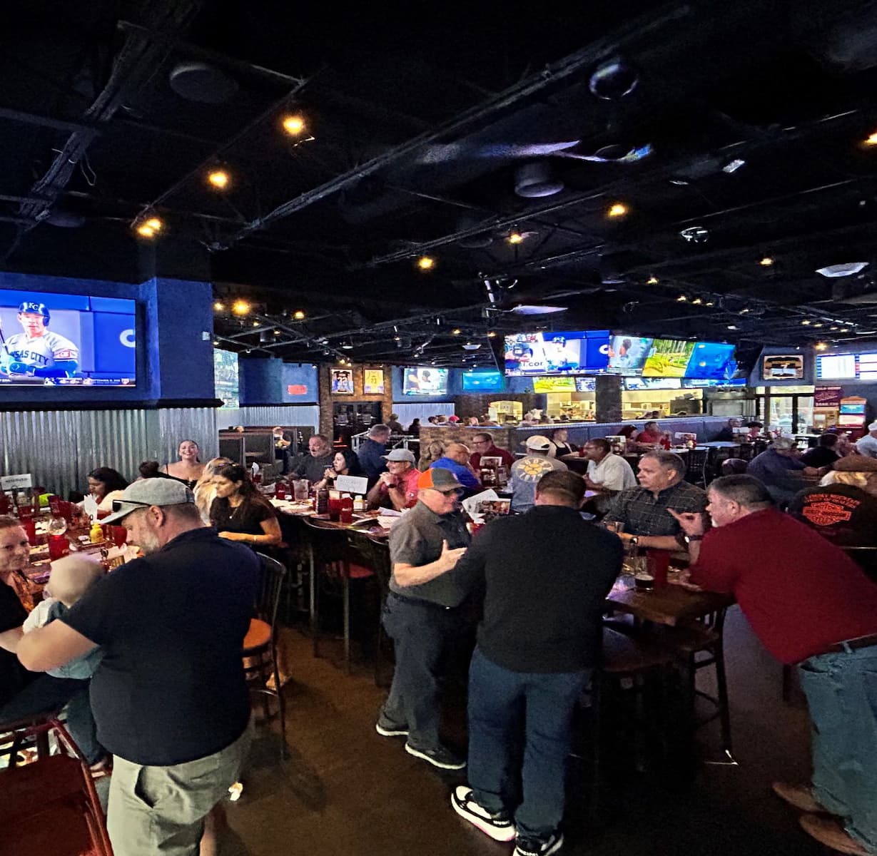 E-Tank Classic post-golf networking event at a local sports bar with teams and clients gathered for food, drinks, and conversation under multiple TV screens.