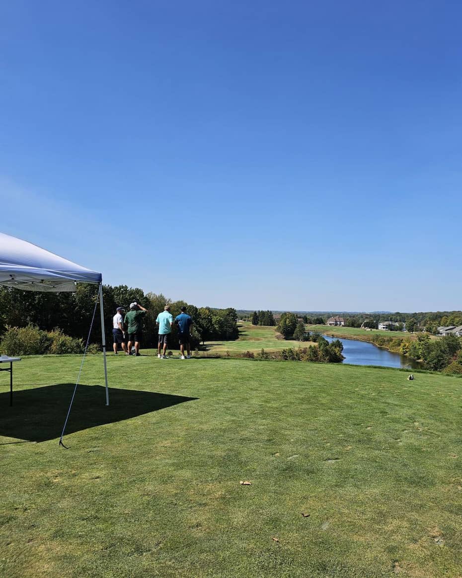 Golfers on tee box overlooking fairway and water feature under clear blue sky at E-Tank Classic charity golf tournament supporting The Legacy Project