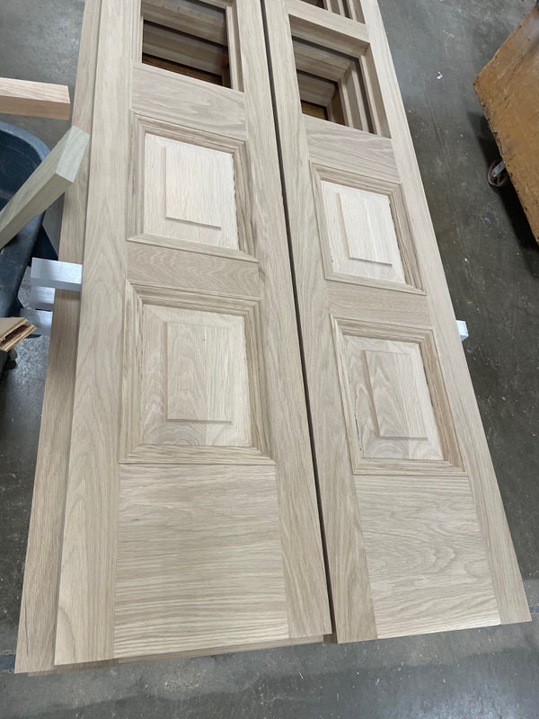 Unfinished custom White Oak double doors with raised panels and glass lite openings, built by Rockwood Door & Millwork for a historic high school restoration project.