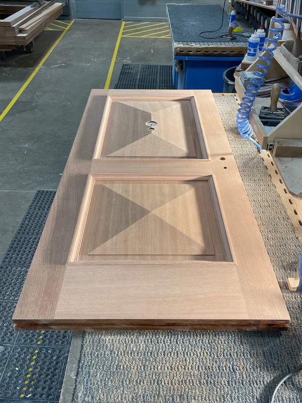 Custom Sipo hardwood entry door in fabrication at Rockwood’s workshop, featuring pyramid panel detailing and precision joinery before finishing.