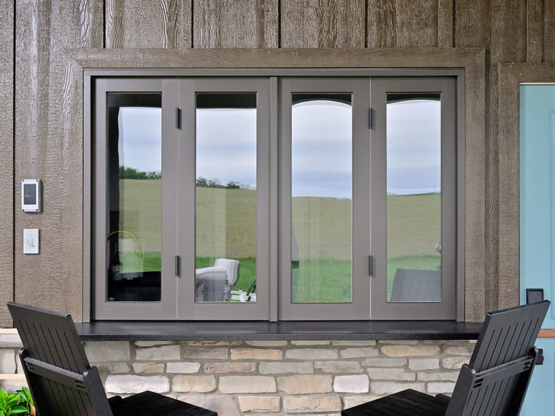 Exterior close-up of a custom pass-through bifold window with gray frame and stone counter at a pool house in Ohio.